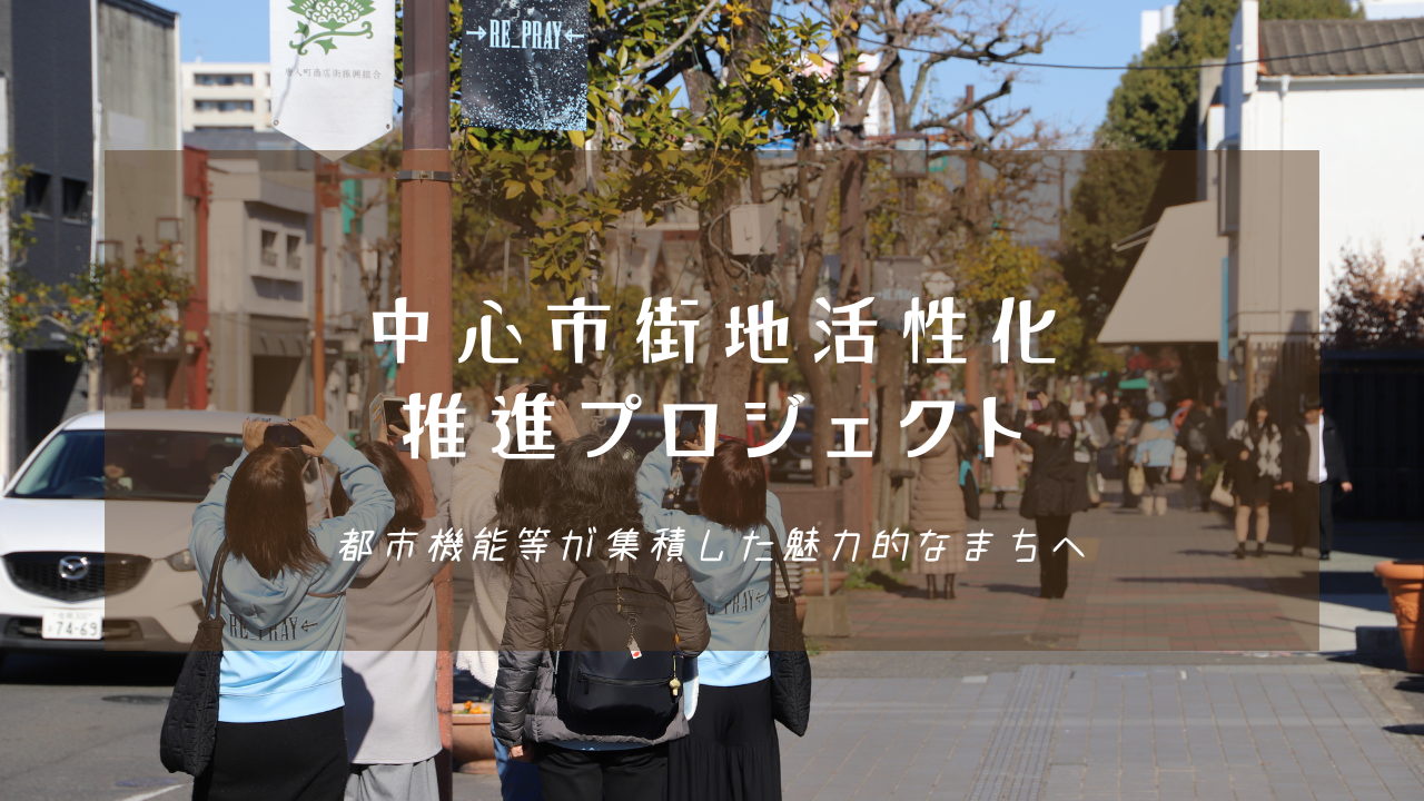 多くの人々が街を歩き、スマートフォンのカメラを構える賑やかな通りを背景に、「中心市街地活性化推進プロジェクト 都市機能等が集積した魅力的なまちへ」という白い文字が中央に配置された写真