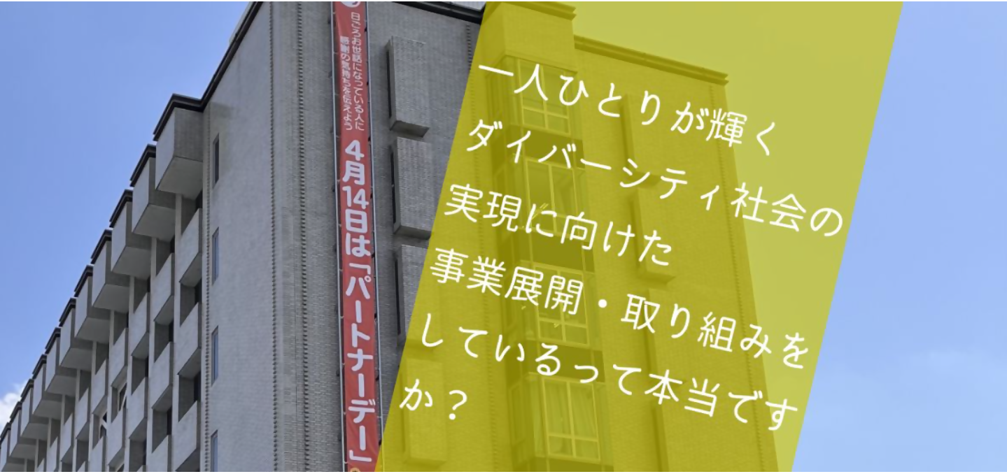 灰色の高層ビルの外壁に「4月14日はパートナーデー」と縦書きで赤い帯に白文字の垂れ幕が掛かり、右側には黄色の半透明な帯に「一人ひとりが輝くダイバーシティ社会の実現に向けた事業展開・取り組みをしているって本当ですか?」という白文字の文章が配置された写真