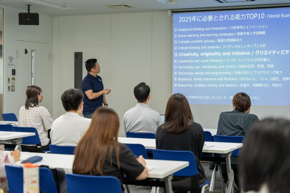 明るい研修室で講師の男性が、プロジェクターに映し出された「2025年に必要とされる能力TOP10」という青いスライドを指し示しながら、着席して真剣に聞き入る受講生たちに解説を行っているセミナーの写真