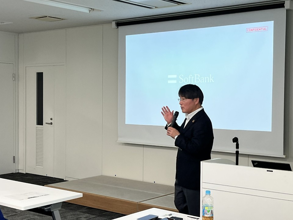 「SoftBank」のロゴが映し出されたスクリーンの前で、男性講師がマイクを手に持ち、身振り手振りを交えながら熱心に話をしているセミナー会場の写真