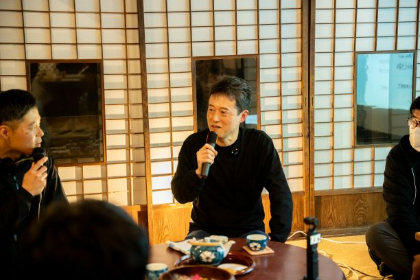 障子のある和室でマイクを手に持ち話している男性を中心に、円卓を囲んで複数の参加者が座談会を行っている様子を捉えた座談会の写真