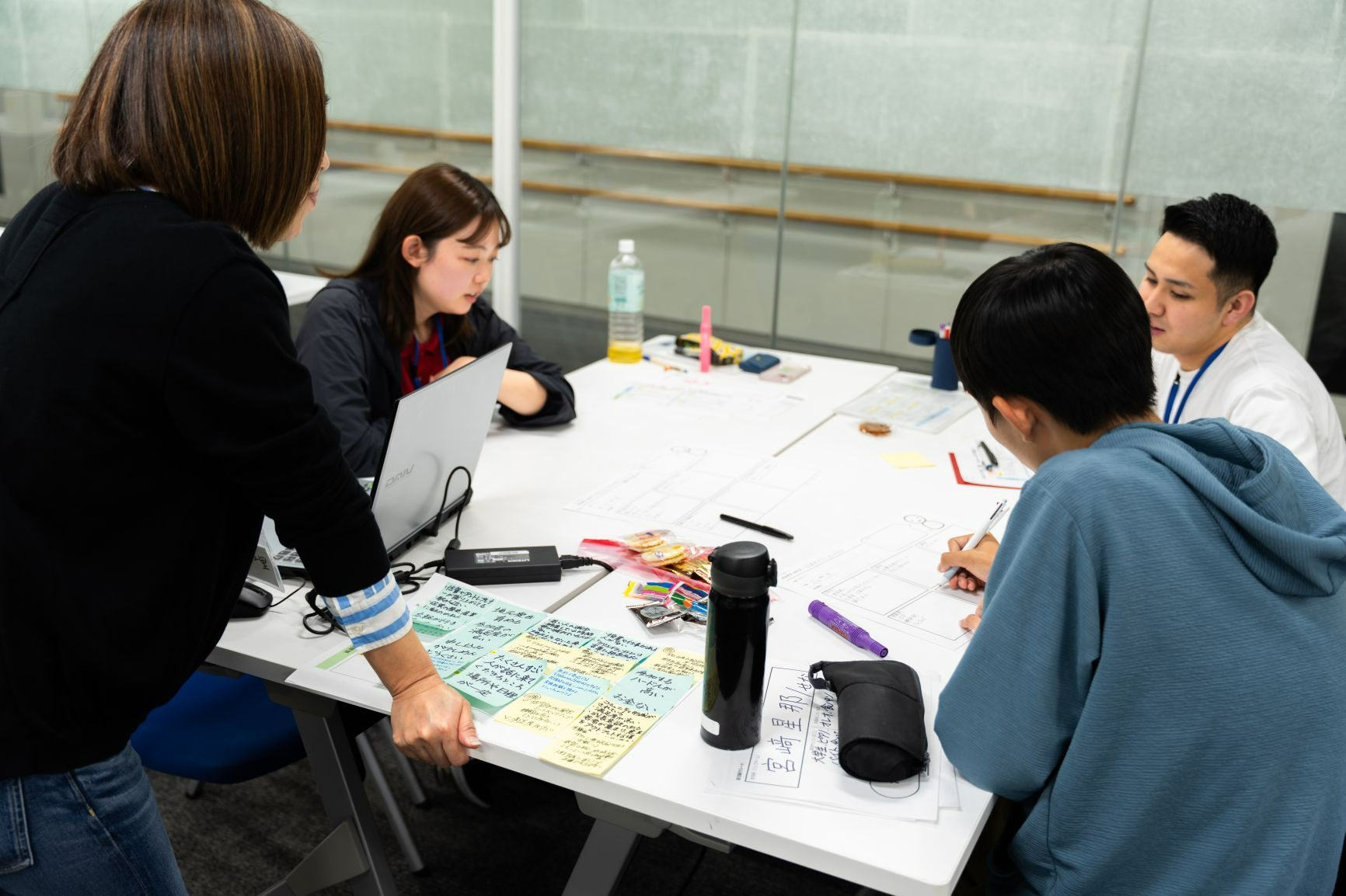 3名の若者が白い机を囲んで向かい合い、企画提案をしている様子の画像