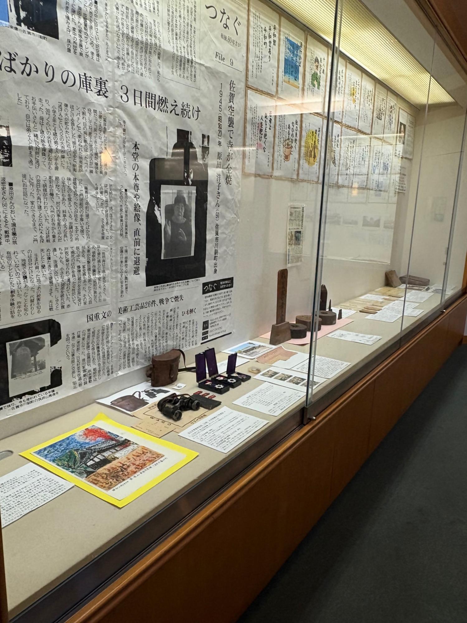 佐賀空襲による寺院の全焼を伝える大きな新聞記事の掲示を中心に、ガラスケース内には双眼鏡や勲章、数々の手記や当時の資料が並べられ、戦争の悲惨さと平和への願いを視覚的に訴えかける展示コーナーの写真