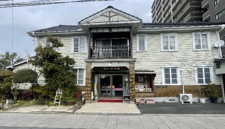 白い木造外壁と中央の玄関ポーチ、二階の小さなバルコニーを備えた趣ある二階建て洋風建物の薮内写真館の写真