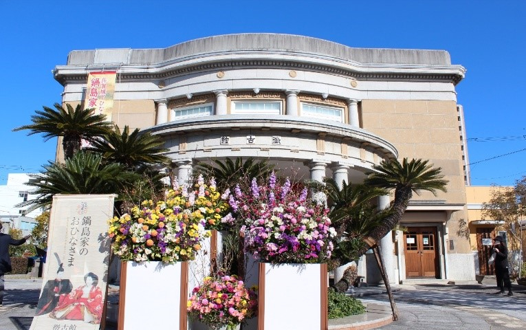 円柱が並ぶ洋風建築の正面に色鮮やかな花々が飾られ青空の下で建物の存在感が際立つ徴古館の写真