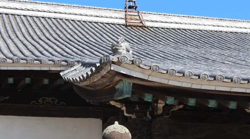 青空の下、曲線を描く瓦屋根と鬼瓦の細かな造形、柱や斗栱の装飾が鮮明に映し出された寺院建築の一部を捉えた写真