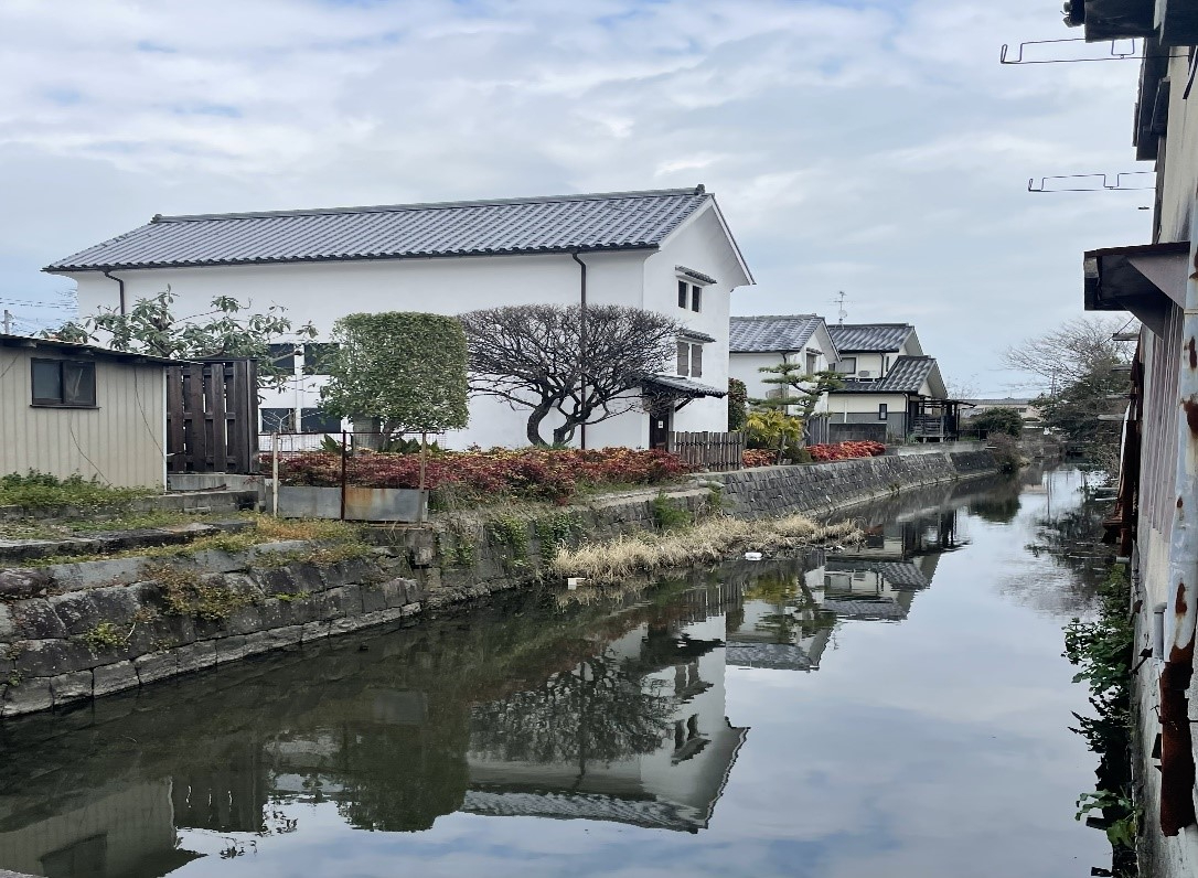 静かな用水路沿いに白壁の家屋と整えられた植木が並び、水面に景色が鏡のように映り込む成就院橋の写真