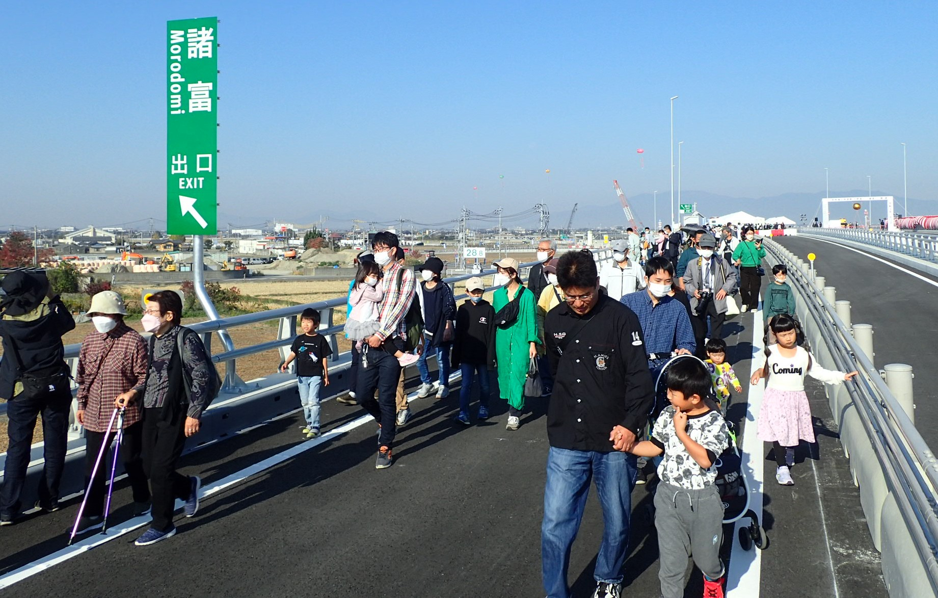 青空の下、新しく開通した道路を多くの人々が諸富出口標識を横目に歩く様子を捉えた写真