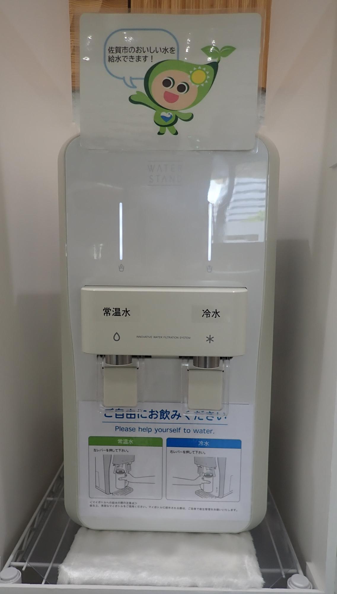 上部には佐賀市のゼロカーボンシティさがしキャラクターこのん が「佐賀市のおいしい水を給水できます!」と話すイラストの案内版があり、下部には使い方の説明が貼られ「常温水」と「冷水」の2つの注ぎ口があるマイボトル専用の白いウォーターサーバーの正面写真
