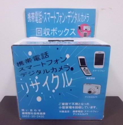 正面に携帯電話、スマートフォン、デジタルカメラのイラストとリサイクルの文字が大きく書かれた、家庭で不要になった小型家電を回収するための青色を基調とした専用の回収ボックスが置かれている写真