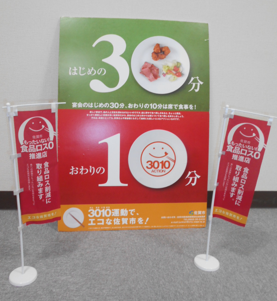 緑と赤の背景に大きく30分と10分の数字が描かれたポスターと、その両脇に「食品ロス削減に取り組みます」と記された赤いミニのぼりが並ぶ、佐賀市の3010運動を周知するための啓発物品が並べて置かれている写真