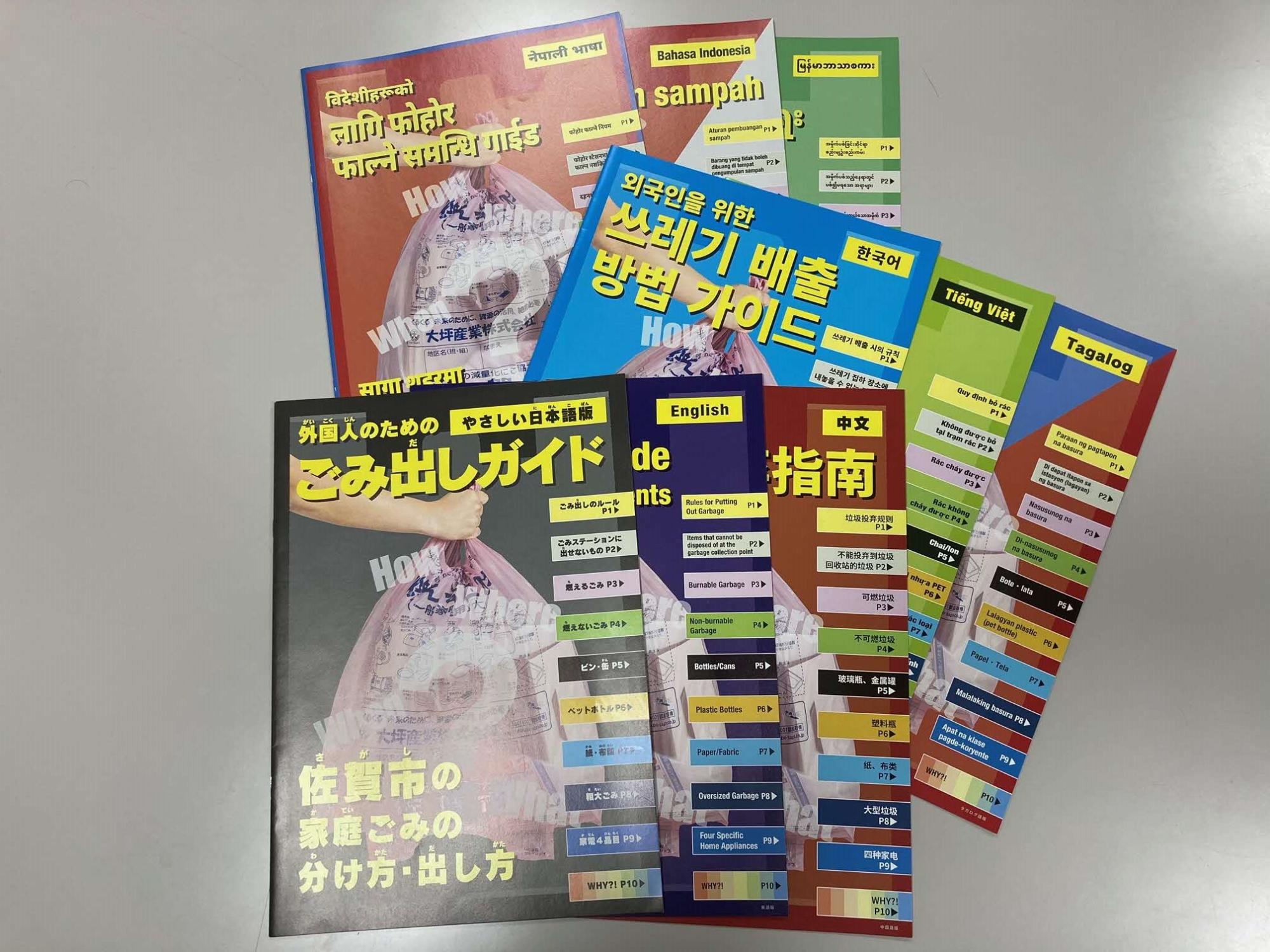 「佐賀市の家庭ごみの分け方・出し方」というタイトルのやさしい日本語版をはじめ、英語、中国語、韓国語、ベトナム語など多言語で作成された「ごみ出しガイド」の冊子が机の上に重なって並べられている写真