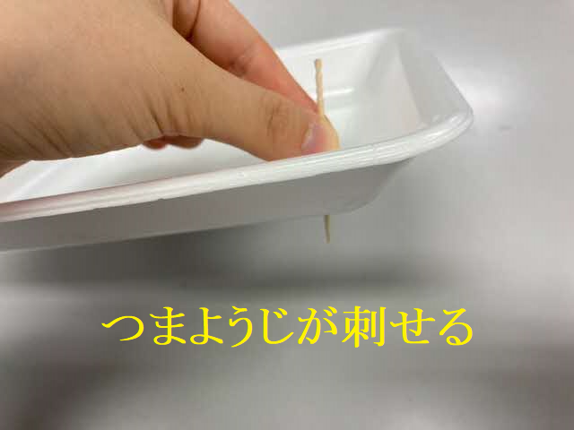 白いプラスチック製の食品トレーの縁に、人間の手が木製のつまようじを垂直に突き刺して貫通させている様子を示し、下部に黄色い文字で「つまようじが刺せる」と書かれた、発泡スチロール素材の判別方法を説明する写真