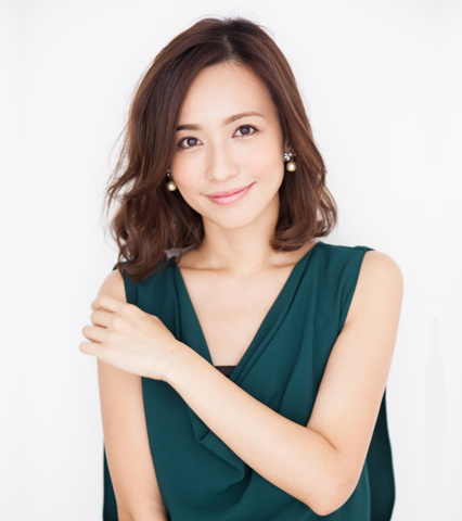明るいベージュの背景に、茶髪でミディアムヘアの微笑む優木まおみさんが深い緑色のノースリーブのトップスを着て、左手で自身の右肩に軽く触れながらこちらを見つめている上半身のポートレート写真