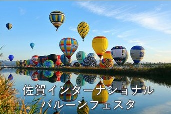 「佐賀インターナショナルバルーンフェスタ」の文字と青い空と穏やかな川面に色とりどりの熱気球が反射するバルーンフェスタの写真