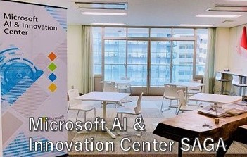 「Microsoft AI & Innovation Center SAGA」の文字と明るい光が差し込む窓際に白いテーブルと椅子が並んでいる室内の写真(Microsoft AI & Innovation Center SAGAのサイトへリンク)