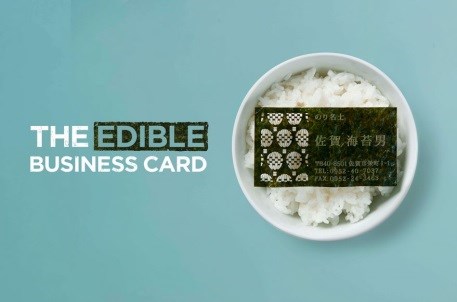 青い背景に「THE EDIBLE BUSINESS CARD」と白い文字で書かれ、右側には白いお茶碗に盛られたご飯の上に、市松模様のロゴや連絡先が刻印された名刺サイズの焼き海苔が置かれているユニークな広告写真