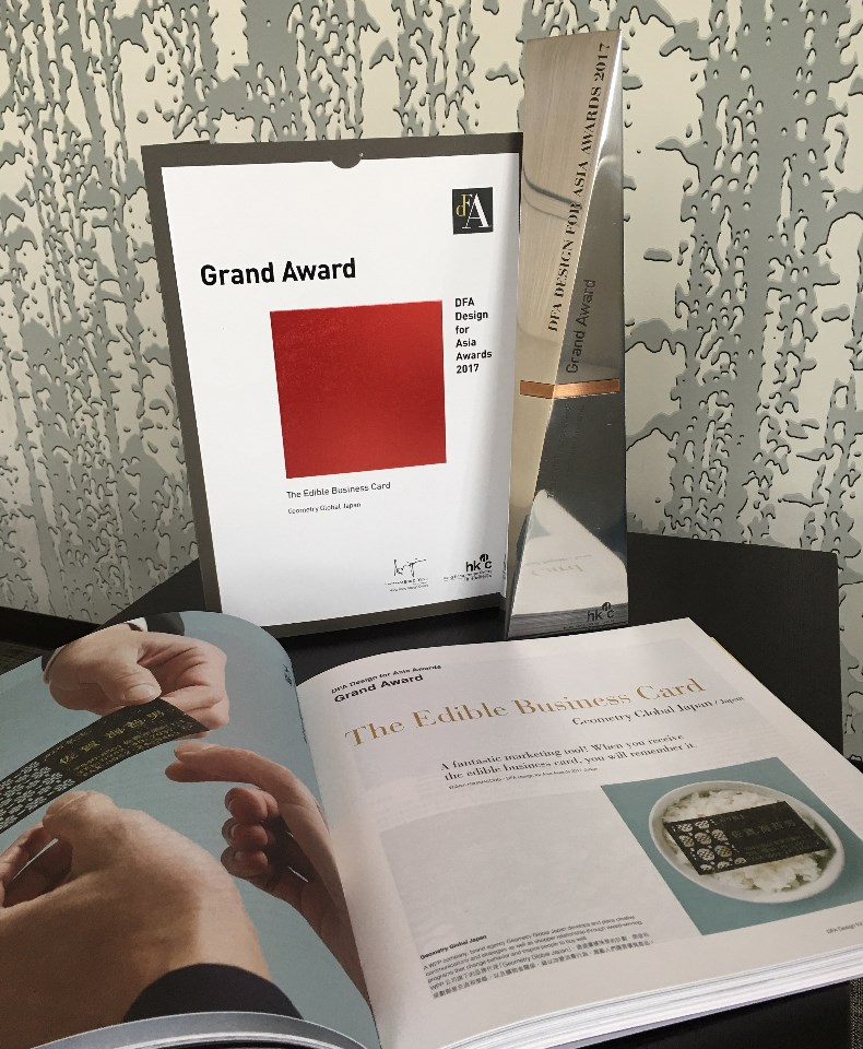 「DFA Design for Asia Awards 2017」の「Grand Award」受賞を証明する赤い正方形が描かれたパネル、細長い銀色のトロフィー、そして「The Edible Business Card」として海苔の名刺を紹介する見開き雑誌が並んだ写真
