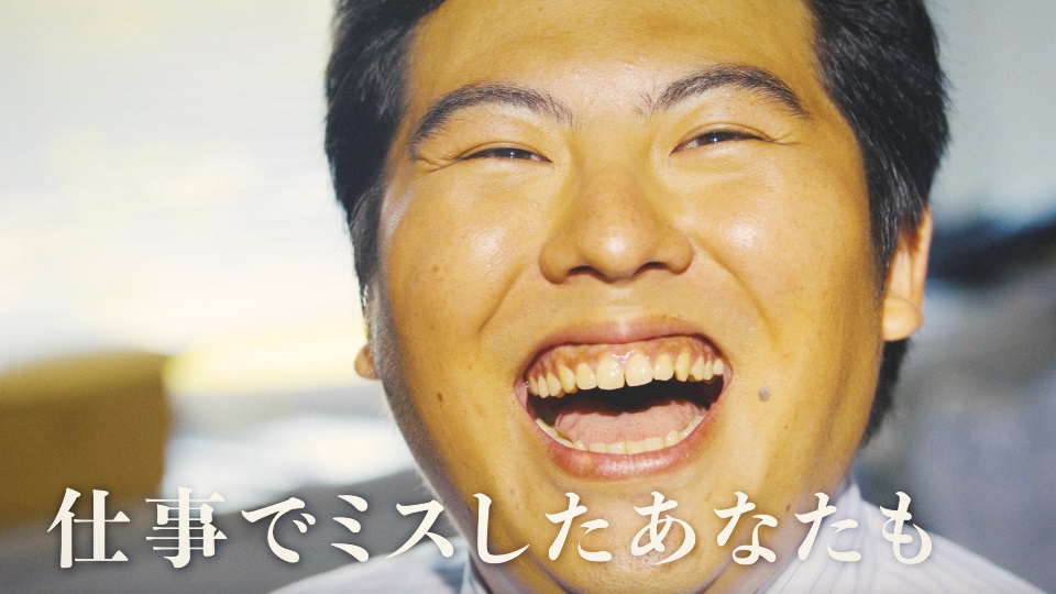 目を細めて口を大きく開け、心からの満面の笑みを浮かべる男性の顔のアップに、「仕事でミスしたあなたも」という白い文字が表示されたスクリーンショット画像