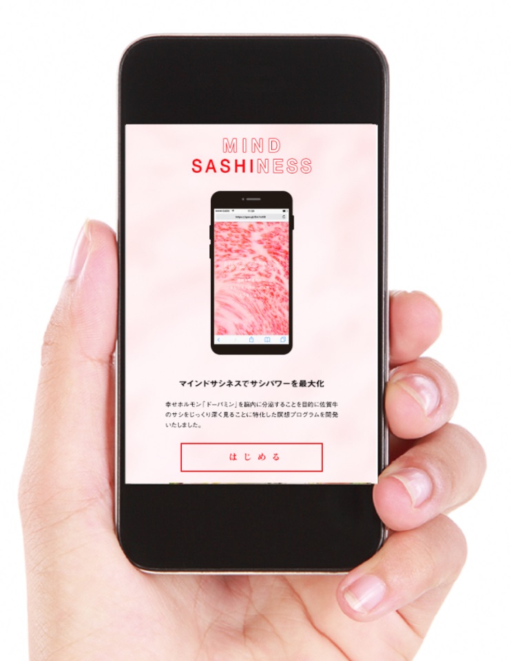 「MIND SASHINESS」というロゴとスマートフォンの画面が表示されたスマートフォンを手に持つ様子が映っており、佐賀牛のサシを鑑賞してドーパミンを分泌させる瞑想プログラムの開始を促すサービス紹介の写真