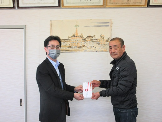 室内で壁に飾られた絵の前に立つ二人が落ち着いた雰囲気で向かい合い、のし袋を両手で丁寧に受け渡す様子を写した写真