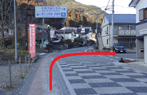 歩道の石畳が続く温泉街の入口付近で右に曲がる進行方向を赤い矢印が示している写真