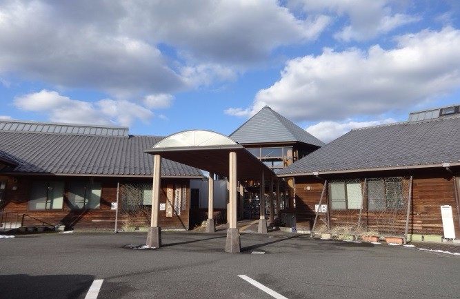 木造の建物の前に白い屋根のエントランス通路が伸び、青空の下で落ち着いた雰囲気を見せる佐賀市立国民健康保険三瀬診療所の外観写真