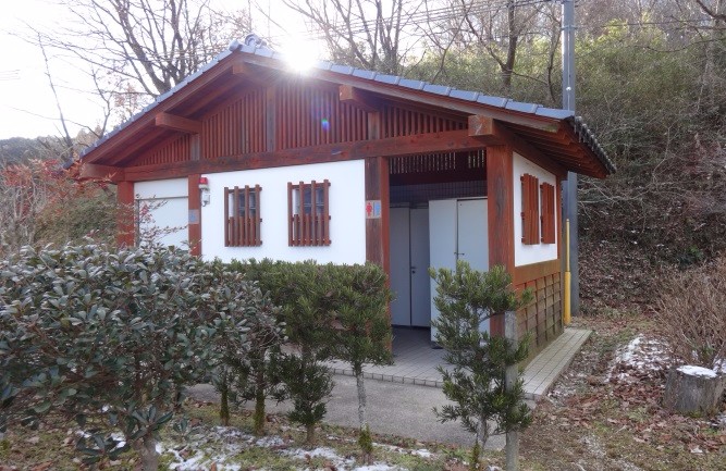 木立に囲まれた敷地に白壁と木枠で造られた小さな和風トイレ棟の写真