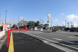 青空の下、歩道から交差点を渡ってセブンイレブンの看板が見える方向へと進むルートを指し示す赤い矢印が描かれ、周囲にはマンションや戸建て住宅が並ぶ日本の郊外の風景を捉えた、道案内の写真