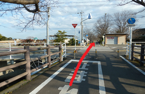 手前に「止まれ」の路面表示があるサイクリングロードから、赤い矢印が横断歩道を渡って直進方向を指し示し進むべき方向を強調した写真