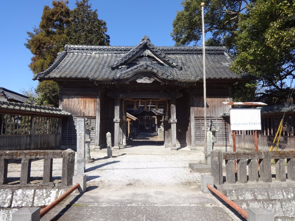 石造りの橋の先に、歴史を感じさせる重厚な瓦屋根と木造の門が構え、門前には石碑や案内板が立ち、奥には注連縄が飾られた社殿がのぞく、晴天の下で厳かな雰囲気を漂わせる西宮社の入り口を捉えた写真