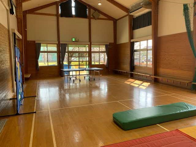 高い天井と大きな窓から光が差し込む室内に卓球台やマットが置かれ広々とした活動空間が広がる写真