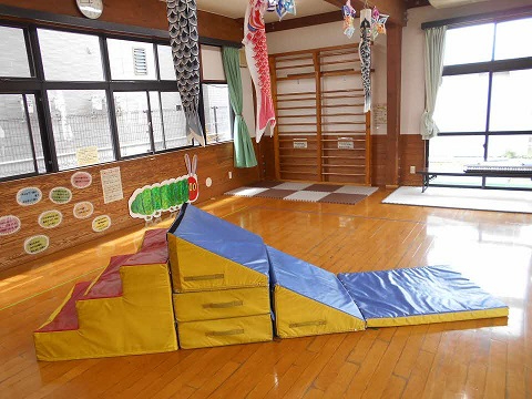 天井にこいのぼりが飾られた大きな窓のある室内に色鮮やかなクッション製の山型遊具が配置された写真