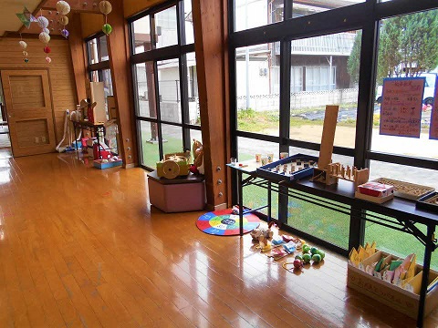 大きな窓沿いに木製玩具やカラフルな遊具が並べられ、明るい廊下に子ども向け遊び場が整えられた写真