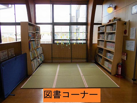 大きな窓から光が差し込む一角に畳スペースがあり、左右の本棚に絵本や児童書が整然と並ぶ落ち着いた図書コーナーの写真