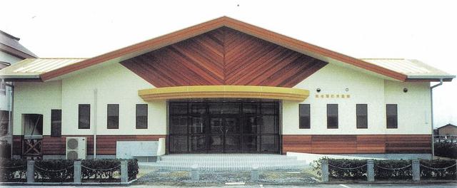 木目模様の三角屋根と白壁を組み合わせた平屋建ての東与賀児童館を正面から撮影した写真