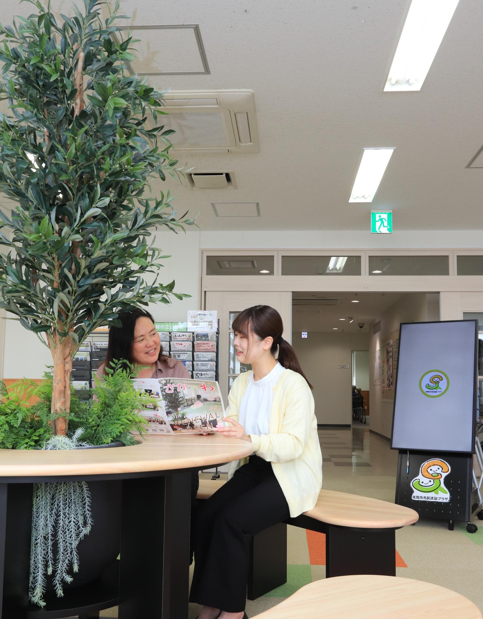 落ち着いた明るい照明の屋内エントランスの円形テーブルで二人がパンフレットを広げて談話する様子の写真