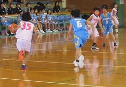 体育館で背番号35の選手がドリブルで前進し、青いユニフォームの守備選手たちが素早く対応する攻防を捉えたバスケットボールの試合写真