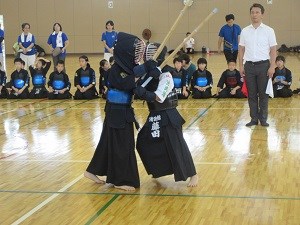 体育館で二人の剣道選手が密着しながら竹刀を振り上げて攻防を続け、周囲の観客が真剣に見守る写真