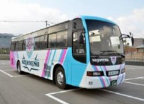 青とピンクのストライプ模様が施され側面に大きく「SAGAN TOSU」と描かれた駐車場に停車中の大型バスの写真