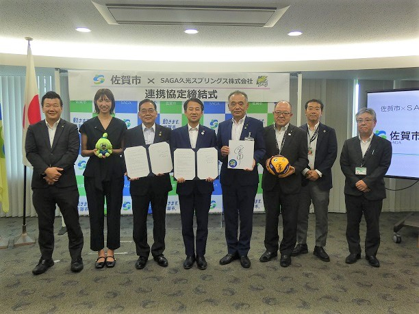 佐賀市と企業の連携協定締結式で関係者が書類や記念ボールを手に横一列に並び記念撮影に応じる様子を収めた写真
