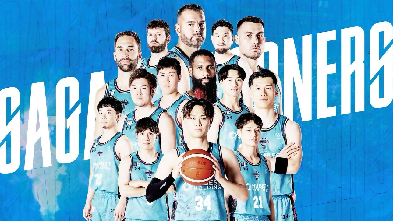 青いユニフォームを着たバスケットボールチームの選手たちが大きなロゴを背に力強く整列する写真