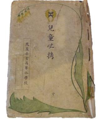 「児童必携」および「芙蓉尋常高等小學校」と縦書きで記された古い冊子の表紙に、黄色い花を咲かせる植物のつるが縁を囲むように描かれた資料写真