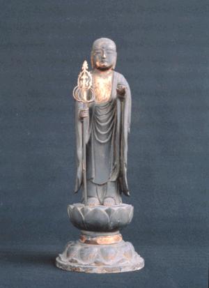 灰色の色調で、右手に錫杖を持ち、左手の掌を軽く上げた姿で蓮華座の上に直立する銅造地蔵菩薩立像を正面から捉えた写真
