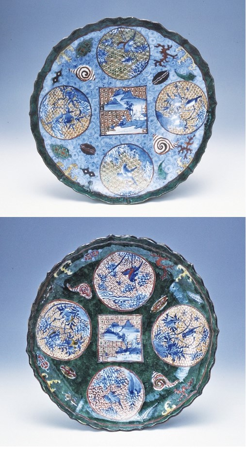 中央の四角い風景画を囲むように、鳥や植物を描いた4つの円形図案と貝殻などの細かな文様が、鮮やかな青色と深い緑色の地に緻密に配置された、波打つ縁取りが特徴的な一対の磁器大皿であり、江戸時代の高い美意識と意匠の凝らされた工芸技術を象徴する、古九谷様式の華やかな磁器の写真