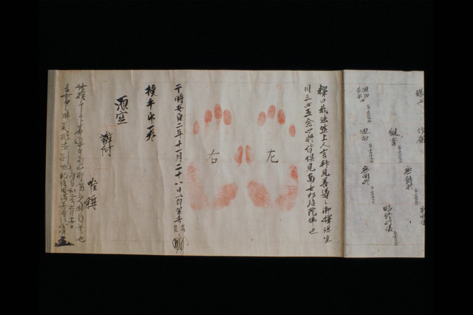薄茶色に色褪せた古い紙の上に、力強い墨書きの漢字とともに、中央に鮮明な赤色で左右一対の手形が押され、その横には日付や人名と思われる文字が整然と記された末代念仏授手の写真