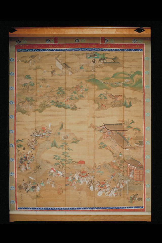 金箔を用いた華やかな縁取りの表装が施され、茶褐色の画面いっぱいに雲の間から覗く社殿や山水、そして下部には神輿を担ぎ行列をなして進む大勢の人々の姿が緻密な筆致で描き出された絹本着彩与賀神社縁起図の写真