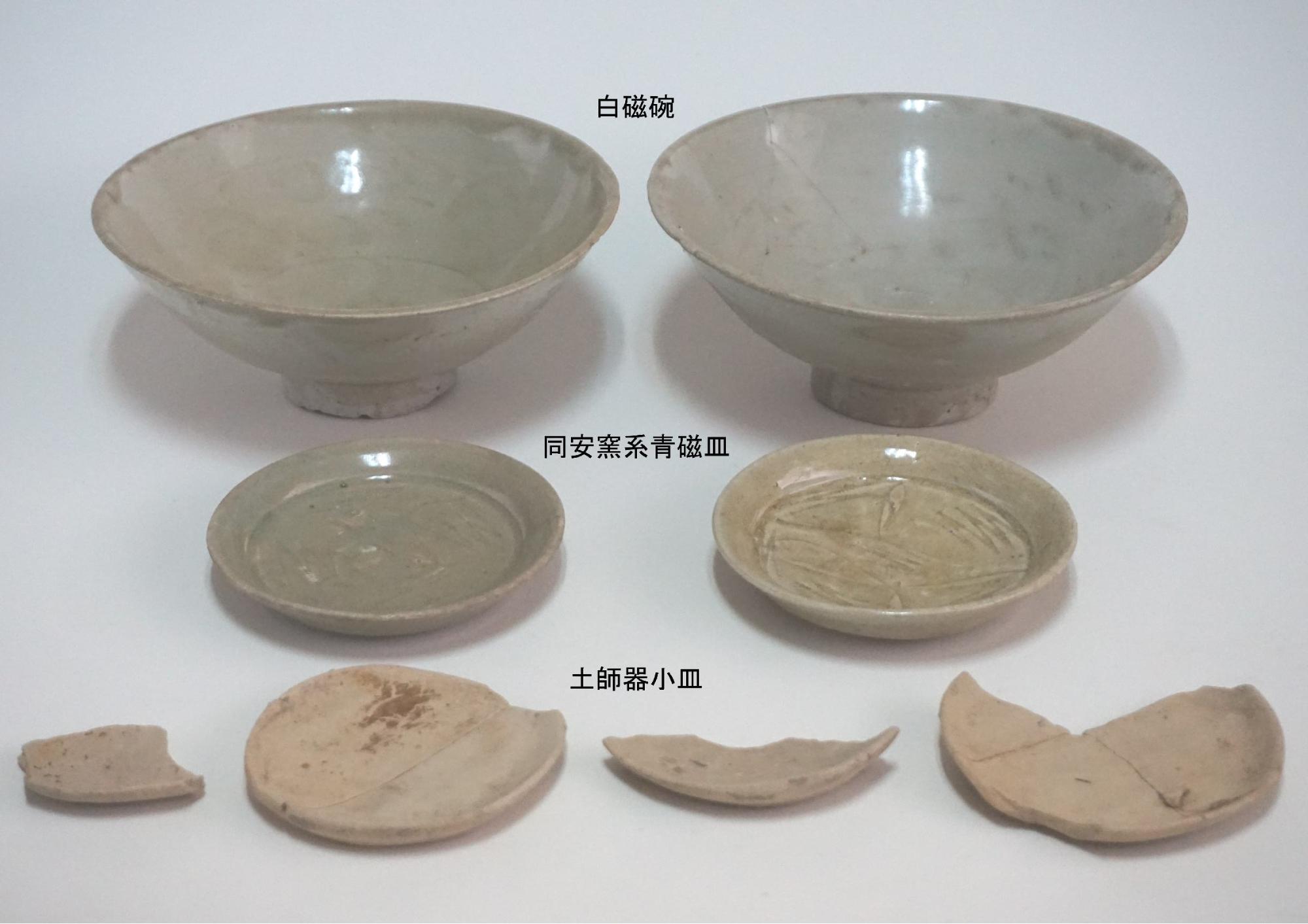 上段には一対の白磁碗、中段には「同安窯系青磁皿」と記された2枚の青磁皿、下段には「土師器小皿」と記された破片を含む4つの土器が整然と並べられた古陶磁器の数々を捉えた写真
