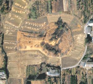 茶色く乾いた大地の中に、鍵穴のような独特の形をした前方後円墳の輪郭がはっきりと浮かび上がり、その周囲をパズルのピースのように不規則な形の田畑が隙間なく取り囲んでいる様子を真上から捉えた航空写真