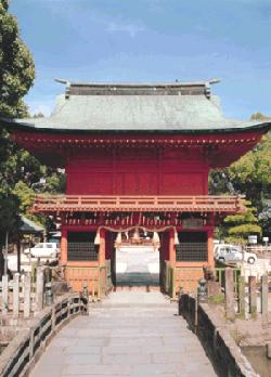 青空を背にした緑豊かな森を背景に、鮮やかな朱塗りの巨大な楼門が石造りの橋の先に堂々と構えており、楼門の重厚な屋根の質感や中央に飾られた注連縄が、日本の伝統的な神社の荘厳さと静謐な美しさを際立たせている、与賀神社楼門の写真
